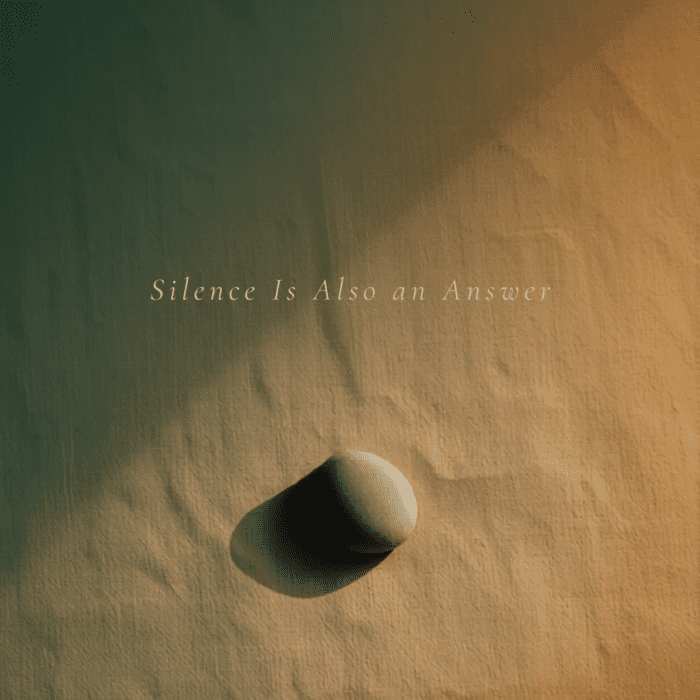 A single smooth stone resting on warm sand in soft golden light, symbolizing silence, stillness, and reflection.